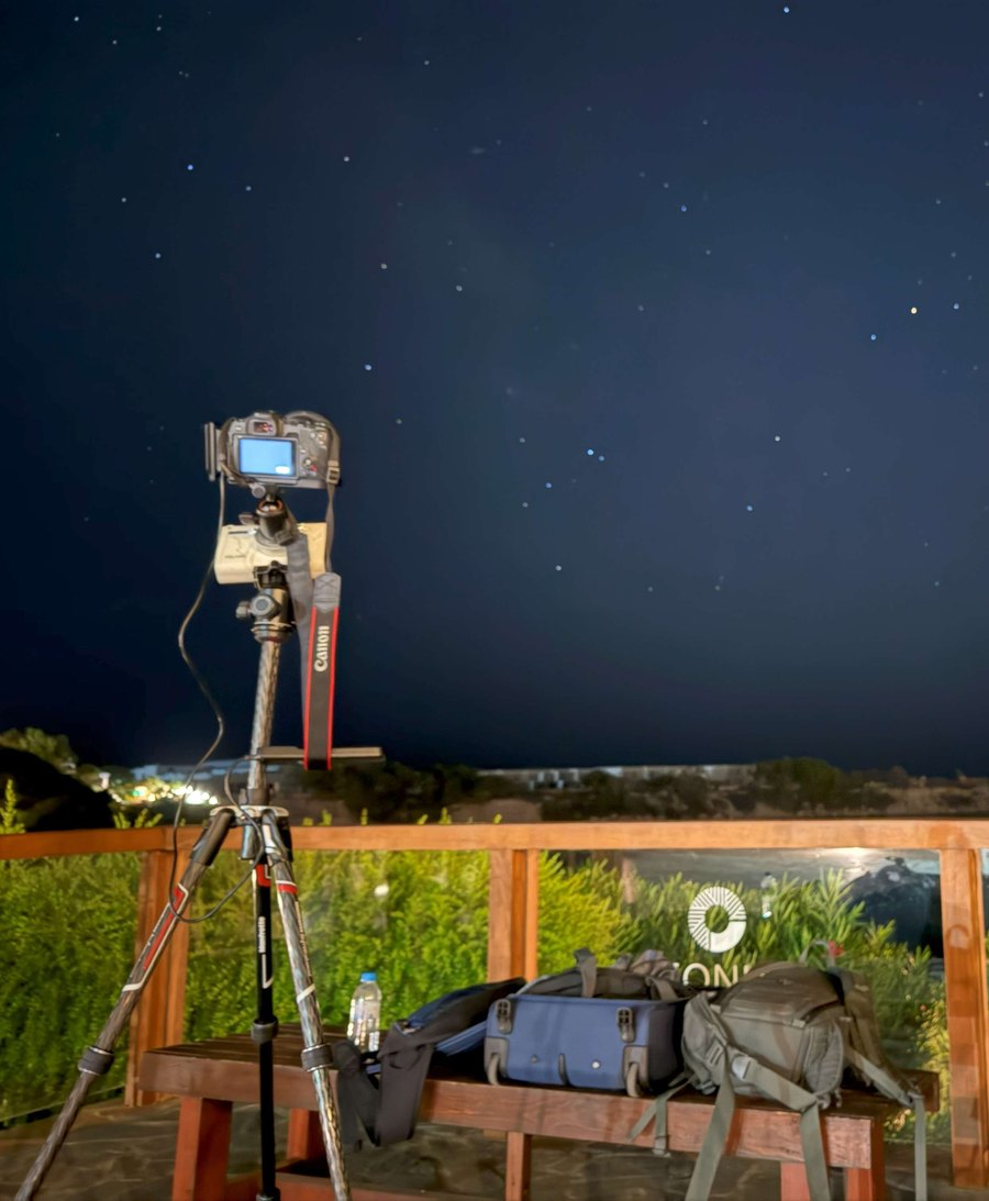 A camera on a small equatorial tracker on a tripod at night, under a starry sky.