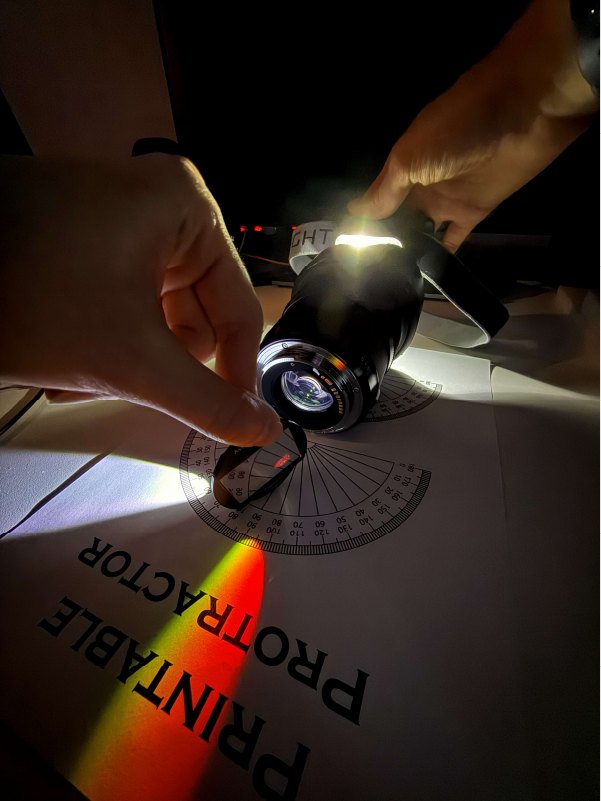 A hand holding a narrowband filter at an angle in front of a white LED, splitting the beam into red and yellow.